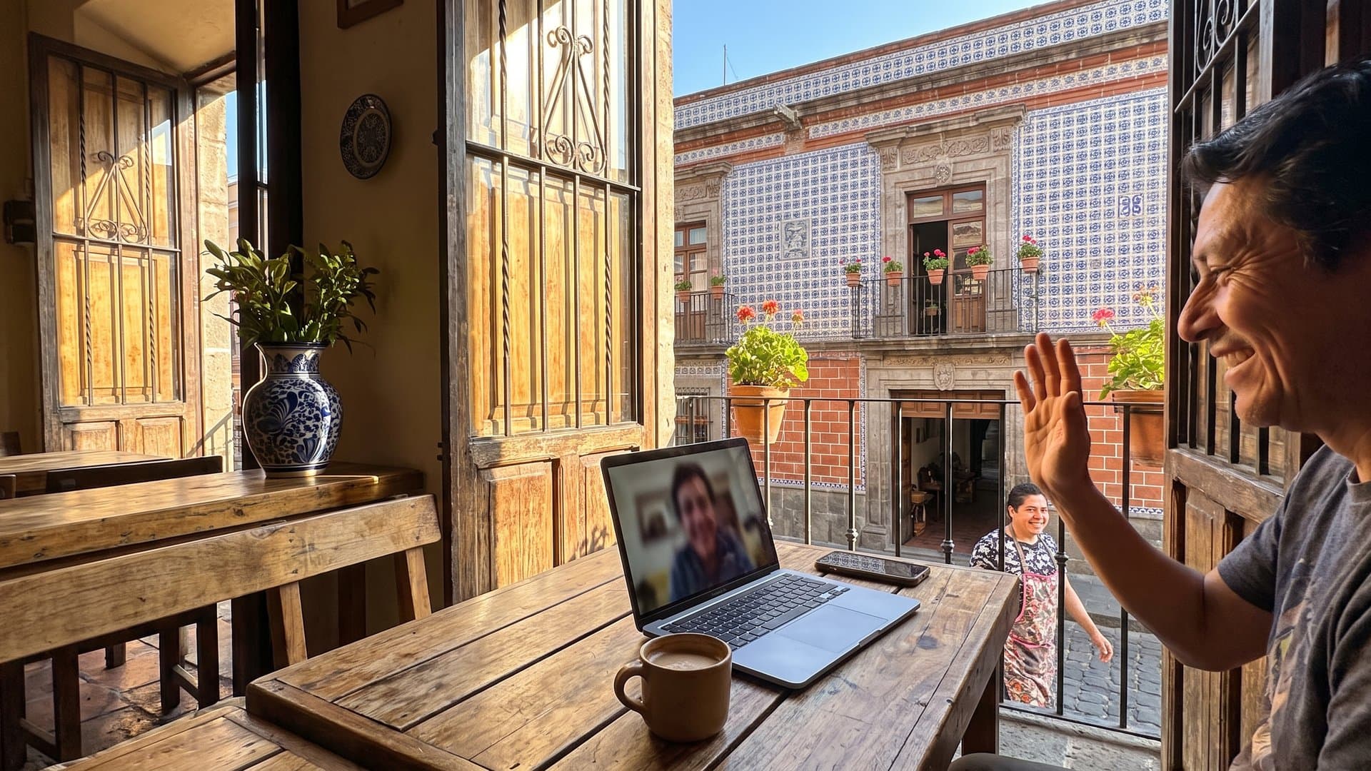 Una mesa junto a una ventana abierta con laptop, celular y un café